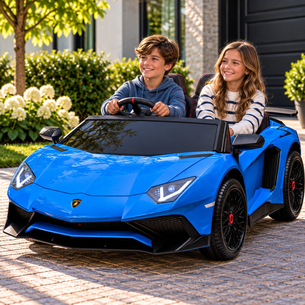 Lifestyle Photo of Two Kids Riding the Blue Lamborghini Aventador XXL 24V Big Kids Ride-On Car on a Home Driveway