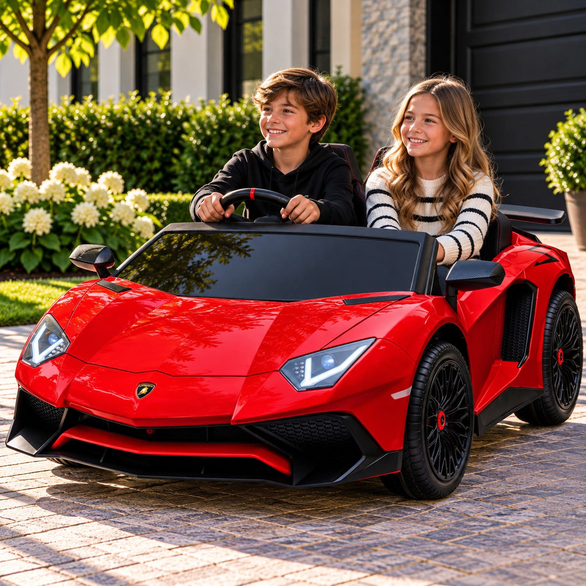 Lifestyle Photo of Two Kids Riding the Red Lamborghini Aventador XXL 24V Big Kids Ride-On Car on a Home Driveway