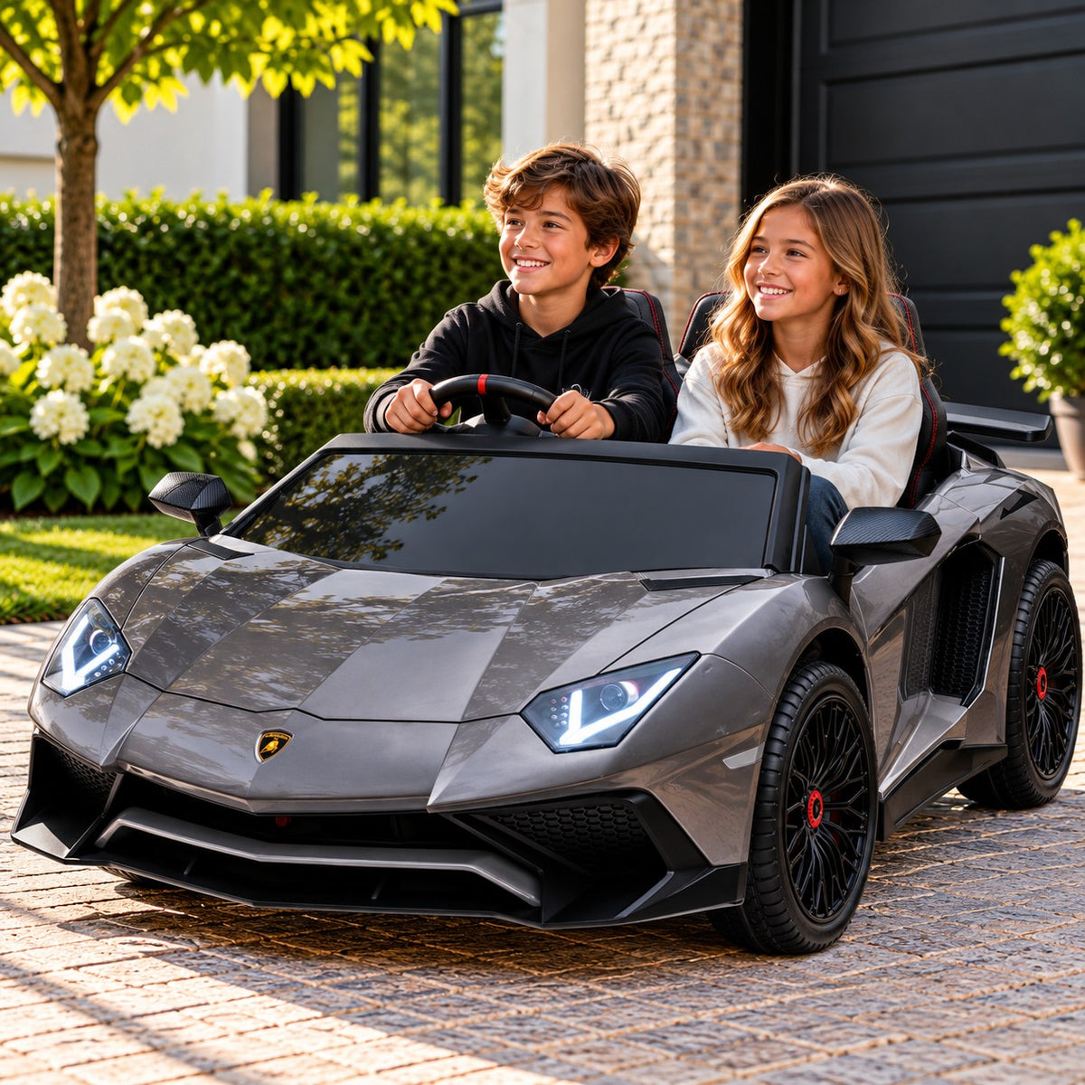 Lifestyle Photo of Two Kids Riding the Gray Lamborghini Aventador XXL 24V Big Kids Ride-On Car on a Home Driveway