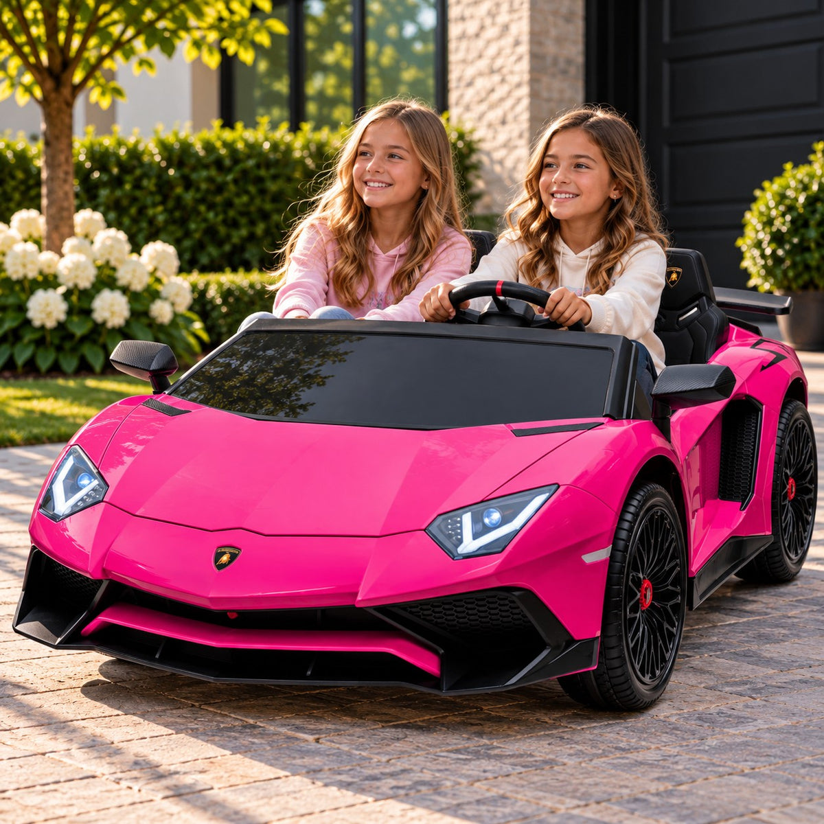 Lifestyle Photo of Two Girls Riding the Pink Lamborghini Aventador XXL 24V Big Kids Ride-On Car on a Home Driveway