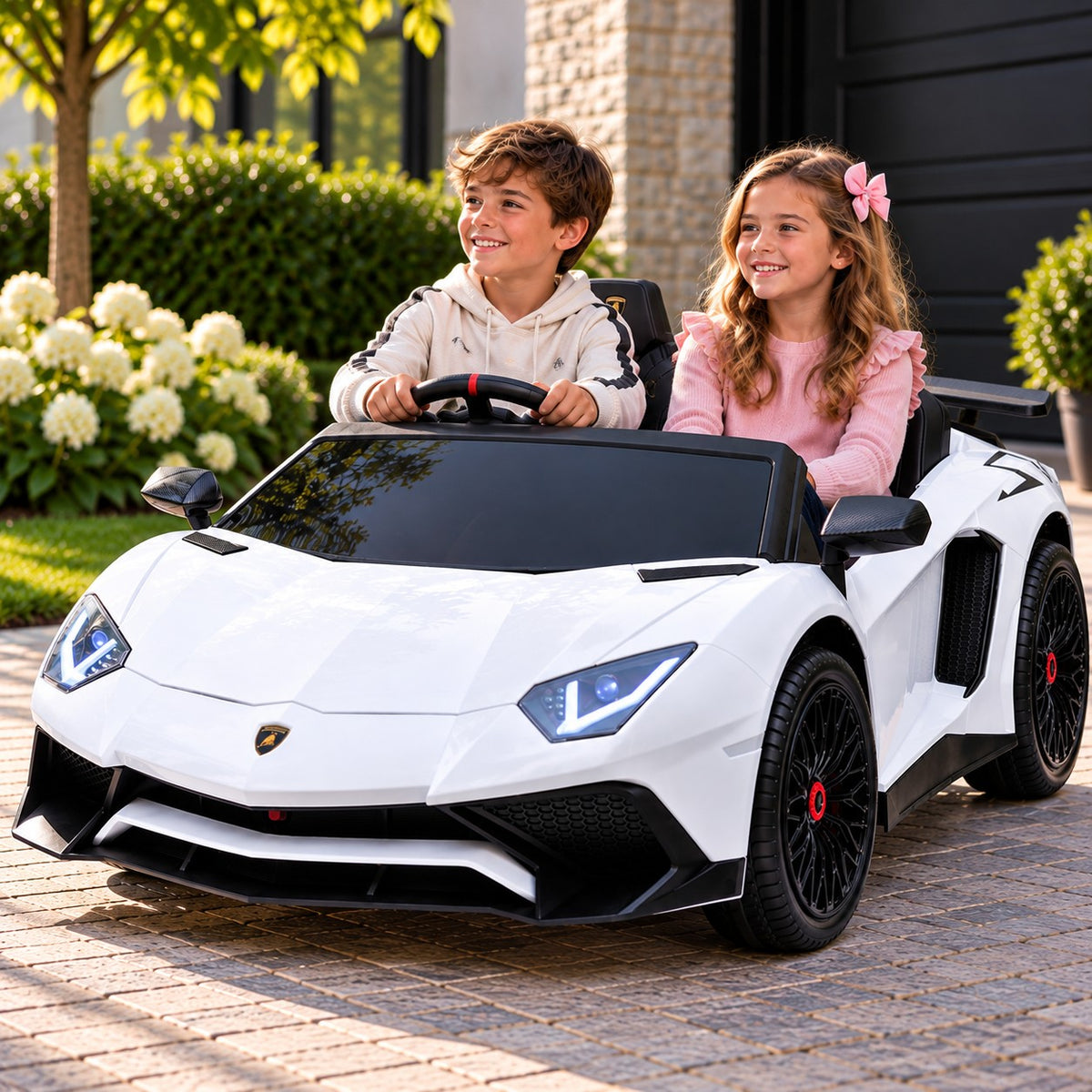 Lifestyle Photo of Two Kids Riding the White Lamborghini Aventador XXL 24V Big Kids Ride-On Car on a Home Driveway